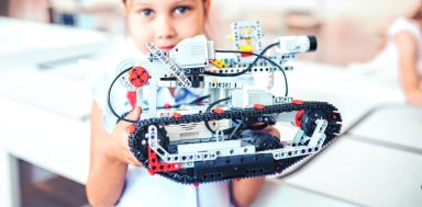 Schoolgirl holding constructor robot in robotics class