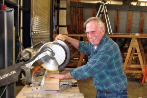 Ida May Project Manager Edward Peterson at home with a saw, cutting a board to size.