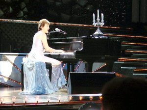 In a gown with a long train she designed and made herself, Feuss performs à la Liberace at the 2006 Senior Ms. America Contest in Las Vegas. Previously, she  was first runner-up in the Senior Ms. New York Contest and was invited to play  and sing at the finals in Las Vegas.