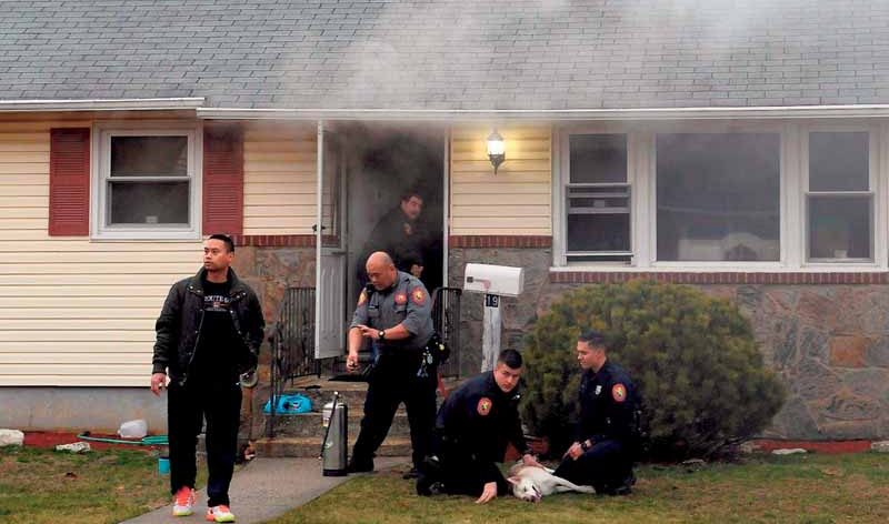 This was the scene at the Georgia Street home of Noah and Jita Klat in Hicksville on Jan. 26 after a fire broke out in the kitchen. Nassau County Police Department Medic Benjamin Butt (in grey shirt) will shortly administer oxygen to the Klat’s dog, Inca, being tended by police officers Andrew Massa (kneeling and looking at camera) and Steven Tornetta, who drove Inca to the nearest veterinarian. In the doorway is Hicksville firefighter and ex-Captain Joseph DiFronzo, who helped rescue two other dogs, hiding under a table in the kitchen. The male at left is an unidentified neighbor. (Photo by Kevin Imm)