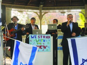 Emcee Dr. Paul Brody is flanked by musical guests Noam Segal playing guitar and guest speaker Dr. Meyer Abittan singing.