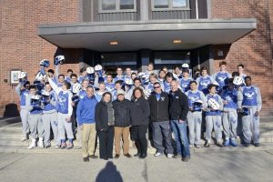 Front row (from left): AAPW Board VP Steve Grossman, Dejana Foundation volunteer Mariann Dalimonte, Dejana Foundation Grant Administrator Jim Avena, Port Washington School District Athletic Director Stephanie Joannon, varsity lacrosse Coach Rooney  and AAPW Board President Peter Smith. Behind them are Schreiber’s varsity boys’ lacrosse team showing off their new helmets.