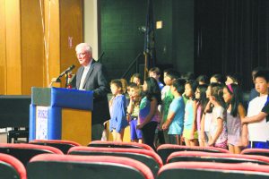 Gereard W. Dempsey Jr. speaks as students from the Roslyn Summer Program stand behind