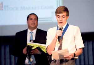 Nikolas Costello ’18 (Bellerose) gives his first place award acceptance speech as  Mr. Jonathan Marron proudly looks on at the finale of the Stock Market Game.