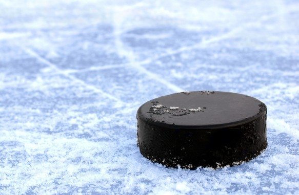 bigstock-black-hockey-puck-on-ice-rink-22755464-583×381