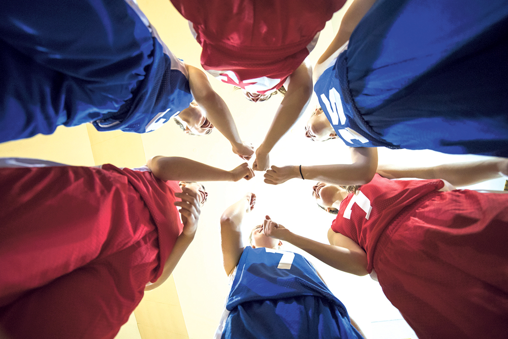 Diverse teenage girl athletes cheering after their team huddle