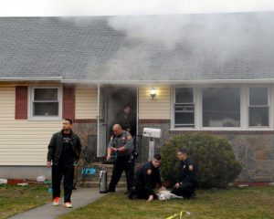 This was the scene at the Georgia Street home of Noah and Jita Klat in Hicksville on Jan. 26 after a fire broke out in the kitchen. Nassau County Police Department Medic Benjamin Butt (in grey shirt) will shortly administer oxygen to the Klat’s dog, Inca, being tended by police officers Andrew Massa (kneeling and looking at camera) and Steven Tornetta, who drove Inca to the nearest veterinarian. In the doorway is Hicksville firefighter and ex-Captain Joseph DiFronzo, who helped rescue two other dogs, hiding under a table in the kitchen. The male at left is an unidentified neighbor. (Photo by Kevin Imm)