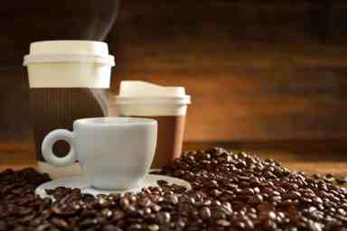 Teacup and saucer and takeaway cups amongst coffee beans