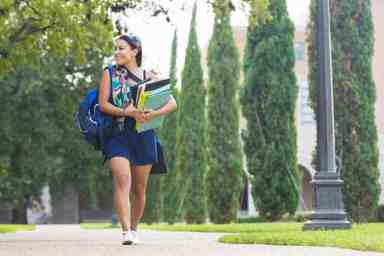 College girl carrying heavy books to class on campus