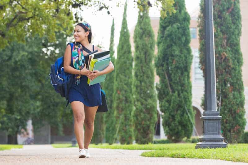 College girl carrying heavy books to class on campus