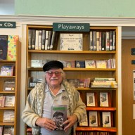 Leonard Lehrman holds his autobiography, "Continuator," in front of the National Music Month display at the Oyster Bay-East Norwich Public Library