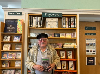 Leonard Lehrman holds his autobiography, "Continuator," in front of the National Music Month display at the Oyster Bay-East Norwich Public Library